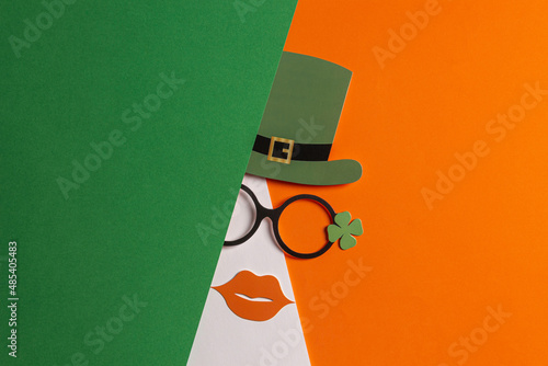 Happy St. Patrick's day background. Patrick day party props: leprechaun hat, glasses with lucky clover trefoil on green white orange background. Decoration of an Irish holiday, March 17