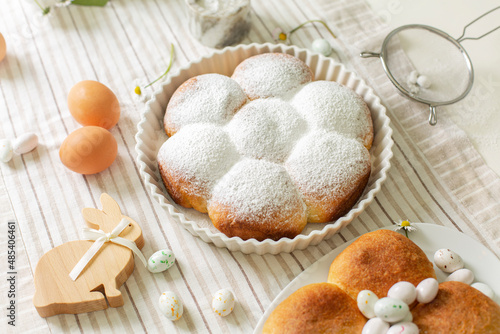 Cooking homemade pastry -  buchtel buns, sweet rolls with jam filling. Easter bunny, eggs, candies and spring flowers on the table. Icing sugar.  Festive preparation. Horizontal image. photo