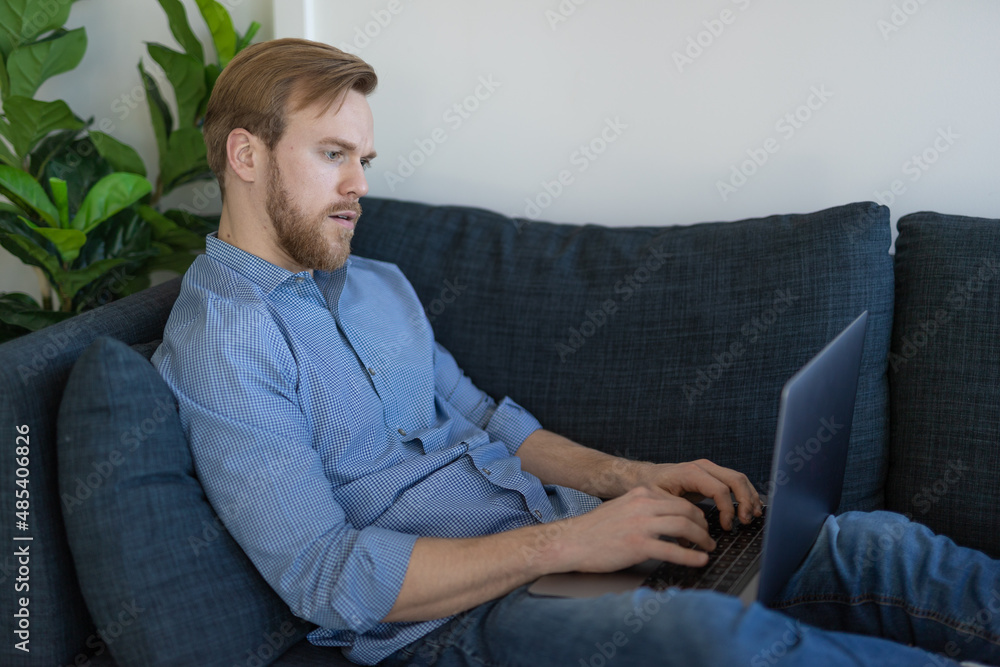 Man at home sitting on a couch using laptop computer