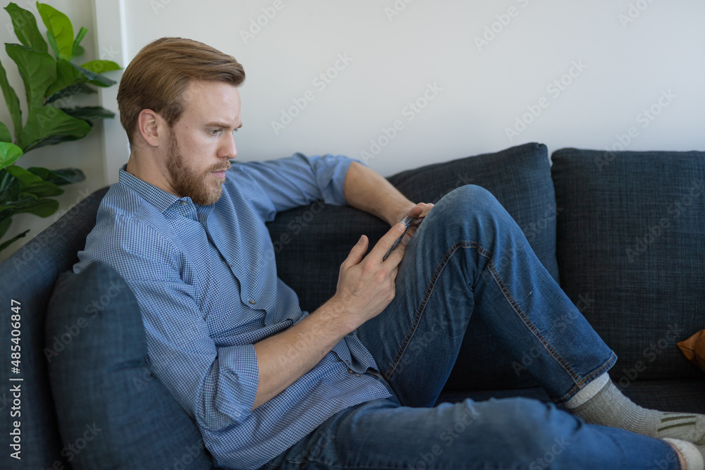 Man at home sitting on a couch using cell phone