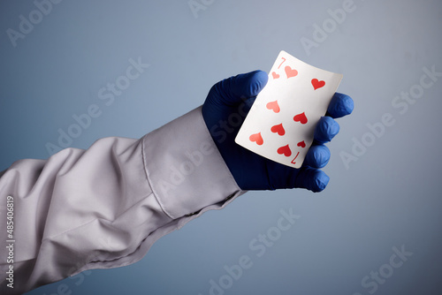 Doctor hand with playing card. Photo with blue gradient background. Hand in white cloth and blue glove shows playing card. Symbol of gambling. Scientist offer gambling game, such as poker.