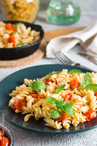 A plate of pasta with tomatoes and basil on a plate and cooking ingredients on the table. Mediterranean cuisine. Vertical view. Close-up