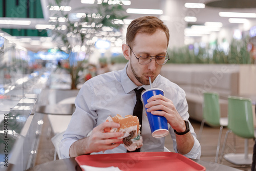 Office worker eating fast food burger and drink soda at food court in mall at lunch