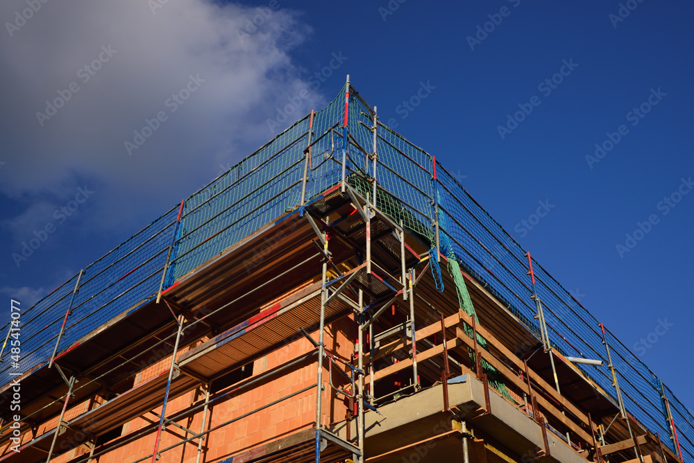 Detail shot from the corner of a freshly laid wall made of bricks, on a construction site, outdoors against a blue sky, with scaffolding on it