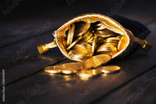 A bag with gold coins on a wooden background. The money is in a black bag. Treasure Hunt