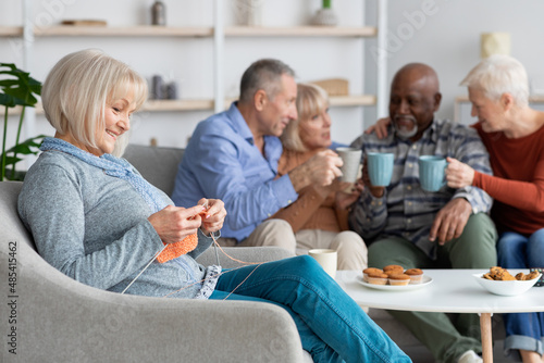 Relaxed senior lady knitting, sitting by her multiracial friends