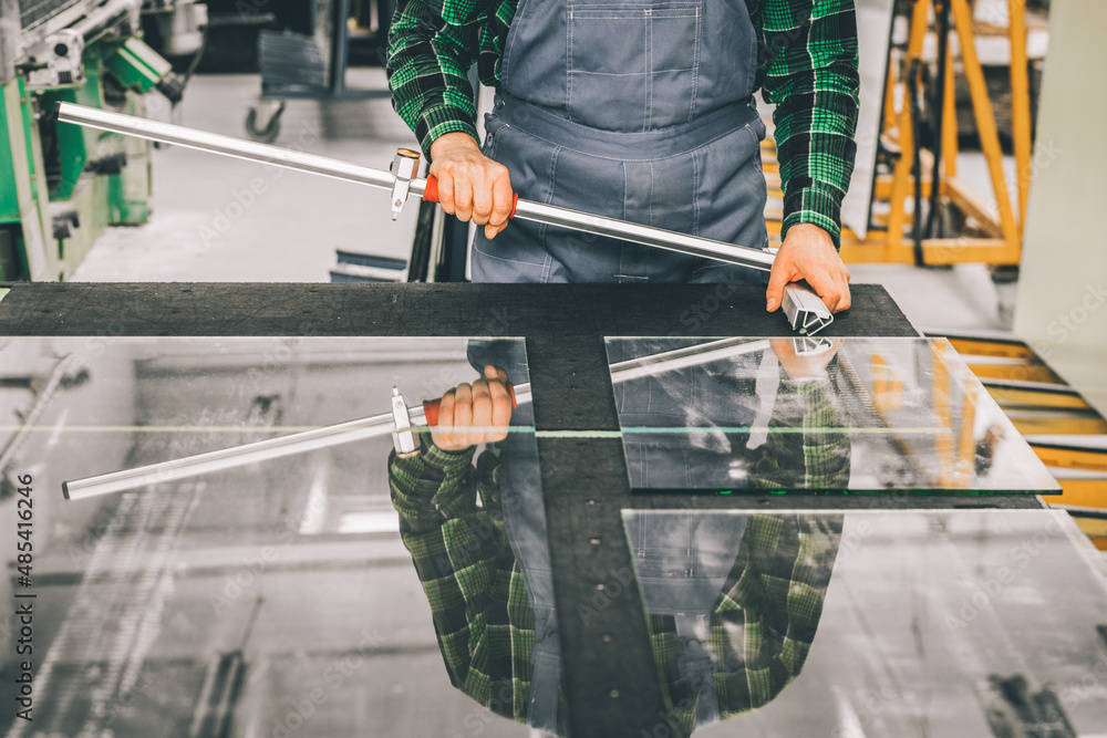 Glazier standing over a cut glass pane with specialized cutting equipment, Cutting glass panels in the factory