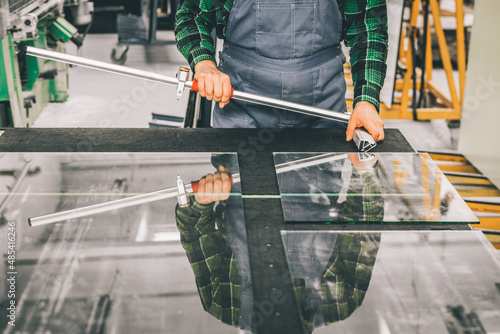 Fototapeta Glazier standing over a cut glass pane with specialized cutting equipment, Cutti