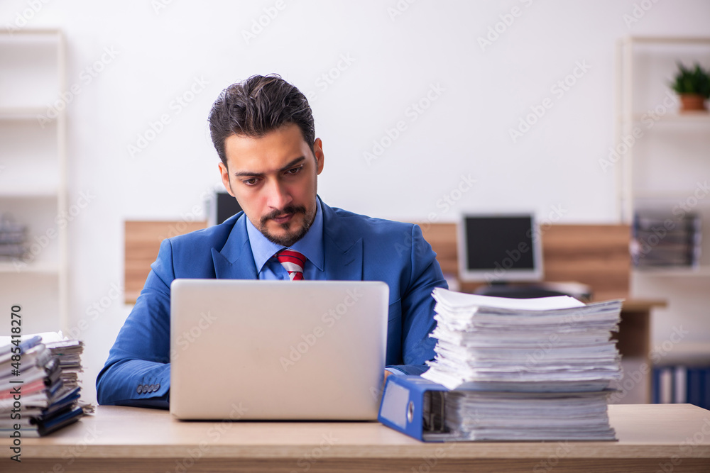 Young male employee unhappy with excessive work at workplace Young male employee unhappy with excessive work at workplace