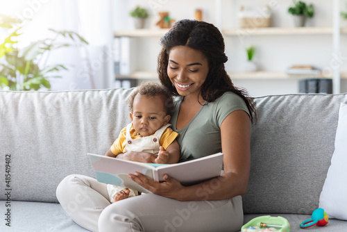 Portrait Of Caring Black Mom Reading Book To Little Baby At Home