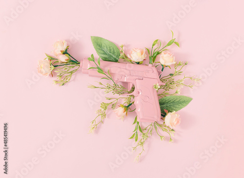 Pastel pink gun with blooming rose flowers and leaves on bright pink background. Minimal peace concept. Creative floral spring composition. Flat lay.