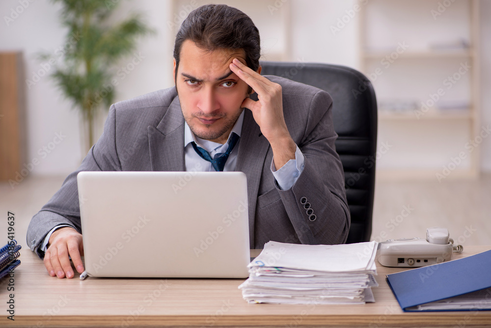 Young male employee unhappy with excessive work in the office Young male employee unhappy with excessive work in the office