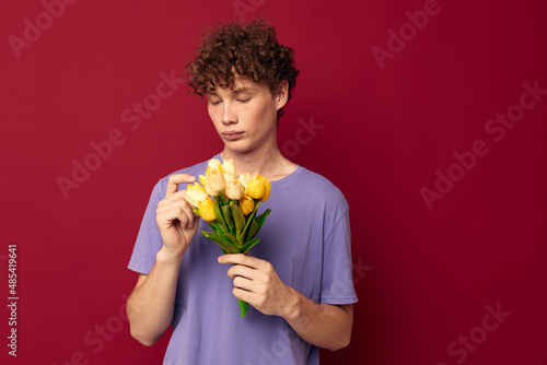 young guy holding a yellow bouquet of flowers purple t-shirts red background unaltered