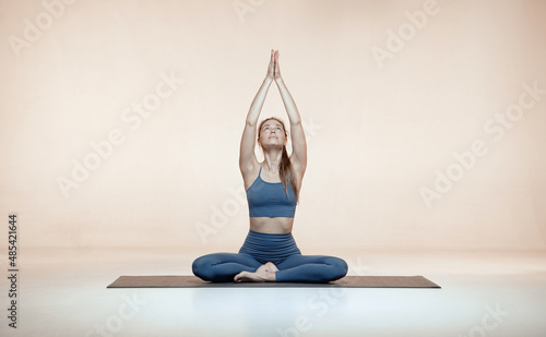 Female yoga coach seated cross-legged in lotus pose or Padmasana make Namaste gesture hands up meditating