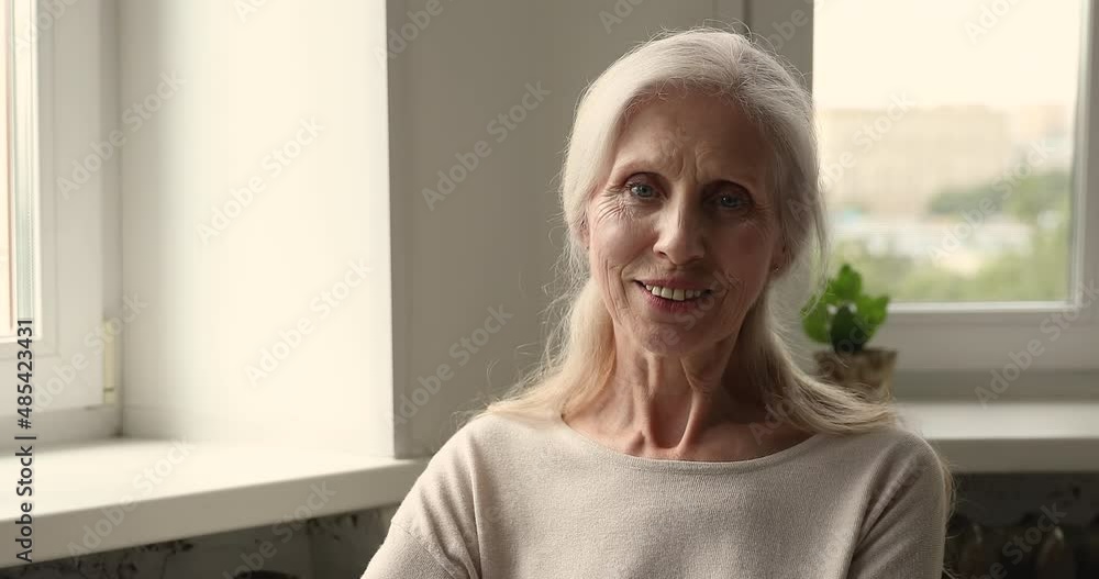 Head shot carefree peaceful older woman sitting alone at home having wide toothy smile looking posing at camera. Good-looking pretty mature grey-haired female, healthy retired person portrait concept Head shot carefree peaceful older woman sitting alone at home having wide toothy smile looking posing at camera. Good-looking pretty mature grey-haired female, healthy retired person portrait concept