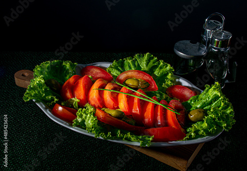salada de alface com tomates em uma travessa branca, em fundo preto photo