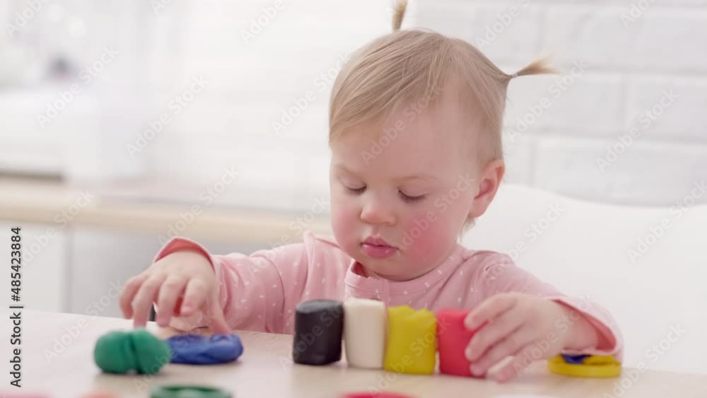 Cute Little girl with funny ponytails on head sitting in kitchen and playing multicolored plasticine, 2 years Kid girl having fun with modeling clay at home, Early education and development Cute Little girl with funny ponytails on head sitting in kitchen and playing multicolored plasticine, 2 years Kid girl having fun with modeling clay at home, Early education and development