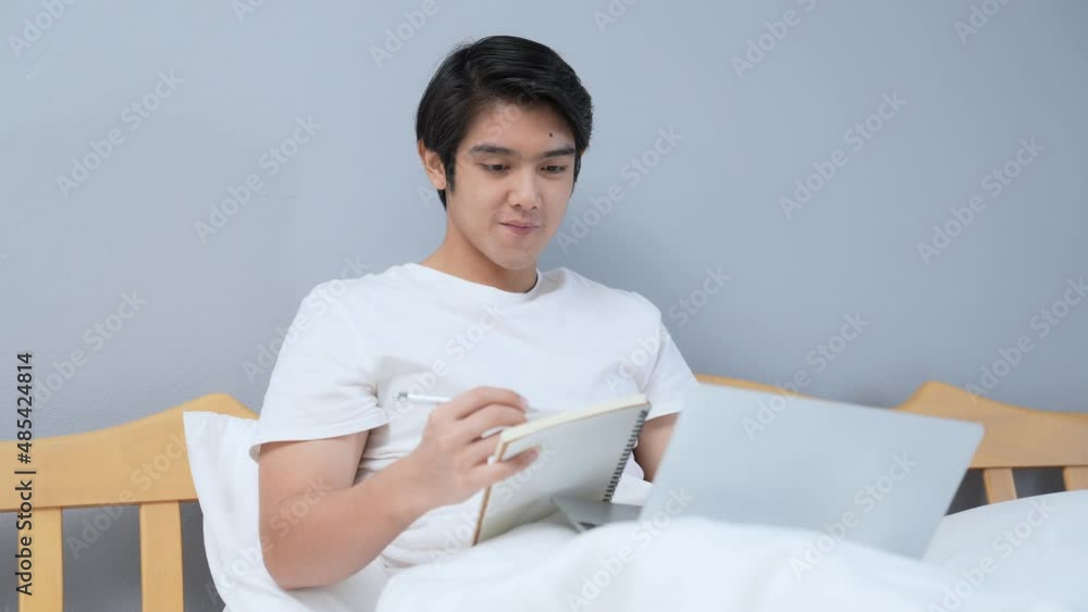 Holiday concept of 4k Resolution. Young Asian man working in the bedroom. taking notes. Holiday concept of 4k Resolution. Young Asian man working in the bedroom. taking notes.