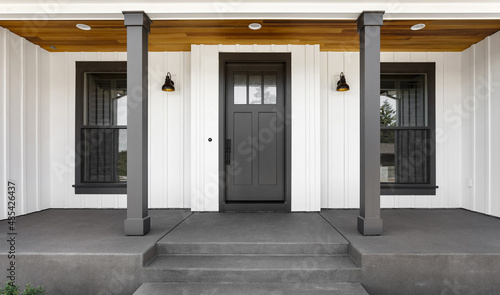 Front door to modern farmhouse home. Home exterior with white vertical wood siding and black front door.  Columns and sconce lights on both sides of door.