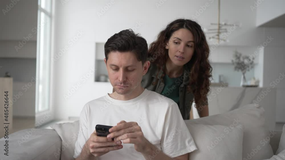 Jealous wife hides behind the sofa and spies on the correspondence in her husband's phone, jealousy and distrust in the family. Jealous wife hides behind the sofa and spies on the correspondence in her husband's phone, jealousy and distrust in the family.