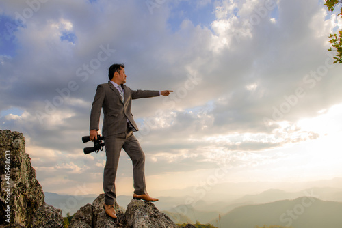 Young businessman using binoculars from a rock over a mountain