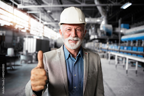 Fotografía Portrait of successful senior factory manager in business suit and hardhat holding thumbs up in industrial production hall