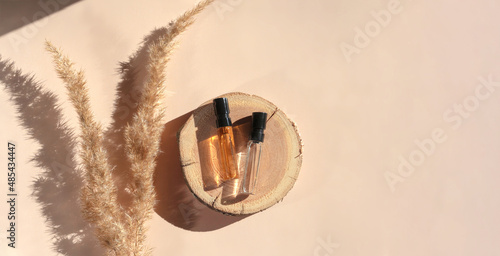 Banner of two Perfume samples with yellow liquid on wooden tray on beige background with pampas grass. Luxury and natural cosmetics presentation. Tester on woodcut in the sunlight. Shades and lights