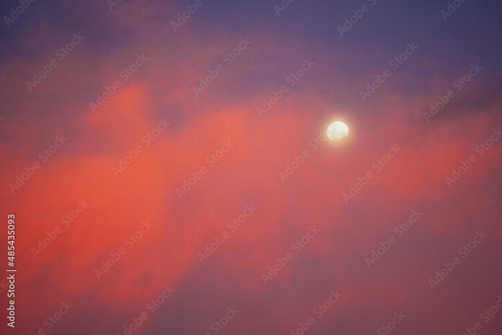 The moon set behind colorful red clouds at sunset