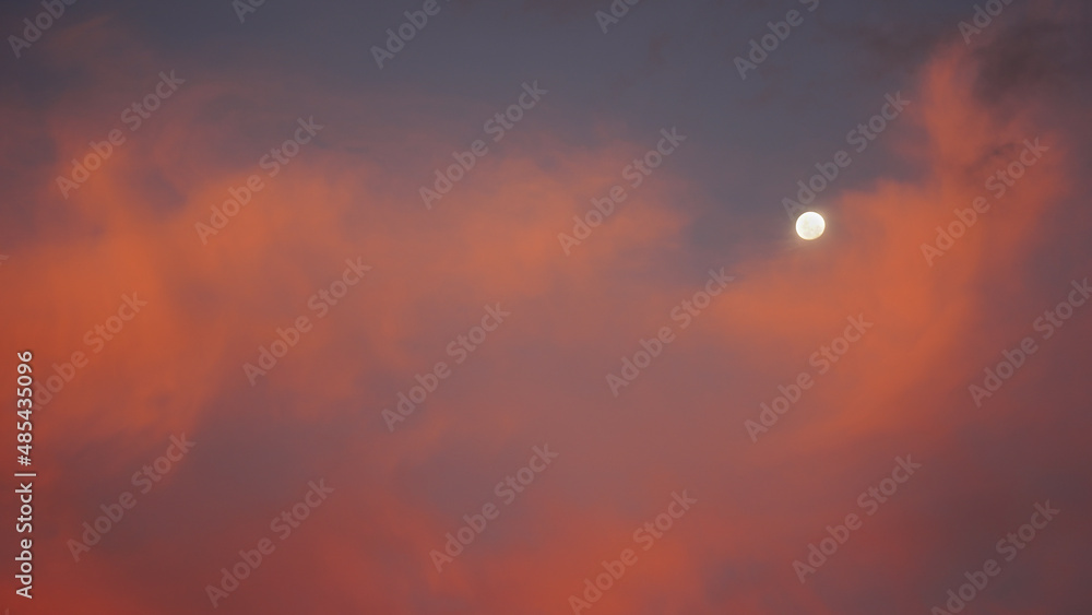 The moon set behind colorful red clouds at sunset The moon set behind colorful red clouds at sunset