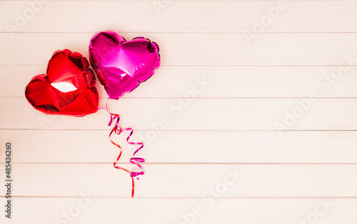 two shiny red and pink heart-shaped balloons with red and pink ribbons on a beige and pink wooden background. Valentine's Day. The 14th of February concept. banner with place for text. copyspace. flat