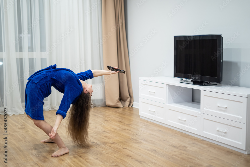 flexible woman exercising at home in front of tv screen, stretching her back. Concept of individuality, creativity and self-confidence