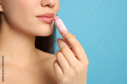 Young woman applying lip balm on turquoise background  closeup. Space for text