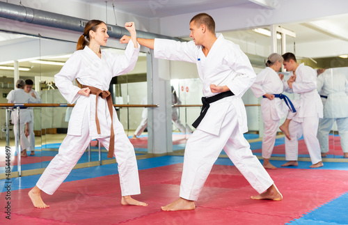 Man and woman in kimono and belt fighting with opponent during group karate training.