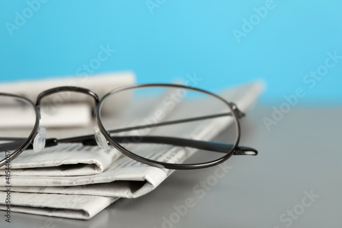 Stack of newspapers and glasses on grey table against light blue background, closeup