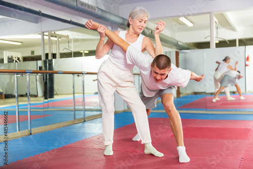 Mature woman performing elbow strike while sparring with man in gym during self-defence training.