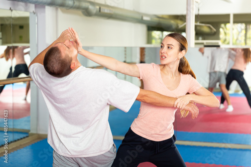 Caucasian woman performing chin strike while sparring with man in gym during self-defence training.