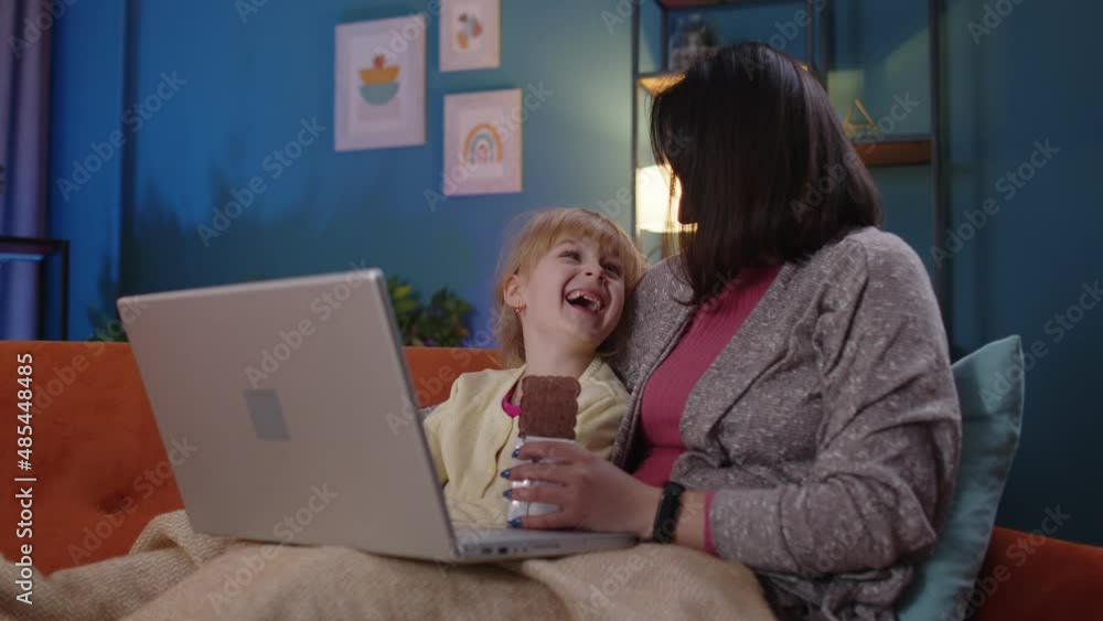 Happy parent mother and cute small child daughter kid looking at laptop screen having fun watching funny study movies or learn together at home relaxing laughing lying on sofa. Family of two people Happy parent mother and cute small child daughter kid looking at laptop screen having fun watching funny study movies or learn together at home relaxing laughing lying on sofa. Family of two people
