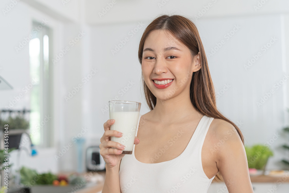 Happy, Asian young woman, girl drinking a glass of white fresh, warm or hot dairy milk for calcium, vitamin wholesome good nutrition in morning at kitchen home. lifestyle, product healthy people. Happy, Asian young woman, girl drinking a glass of white fresh, warm or hot dairy milk for calcium, vitamin wholesome good nutrition in morning at kitchen home. lifestyle, product healthy people.