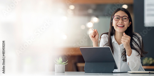 Elegant businesswoman sitting in office with digital tablet. Excited asian businesswoman raising hands to congratulate while working on laptop in office. photo