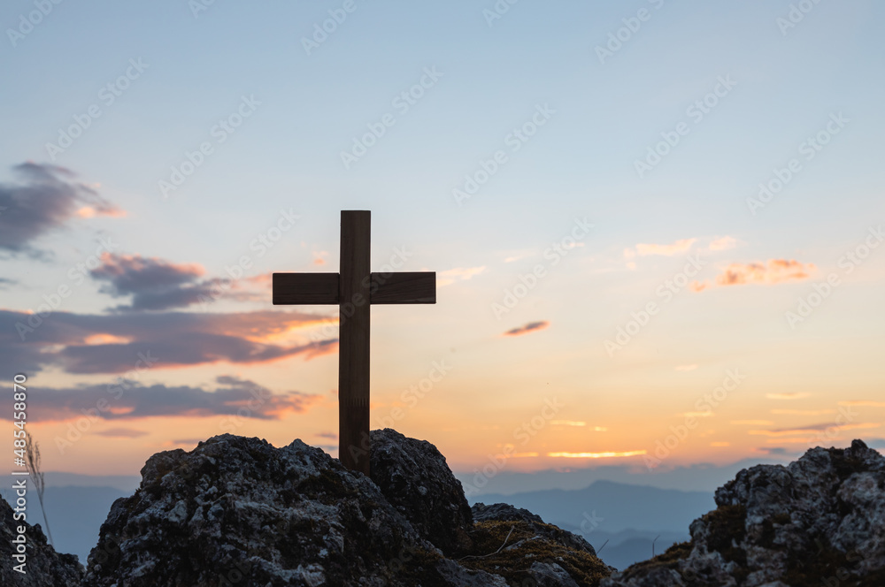 Silhouettes of crucifix symbol on top mountain with bright sunbeam on the colorful sky background