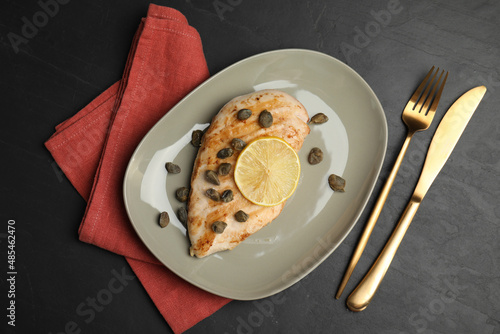 Delicious chicken fillet with capers and lemon served on black table, flat lay