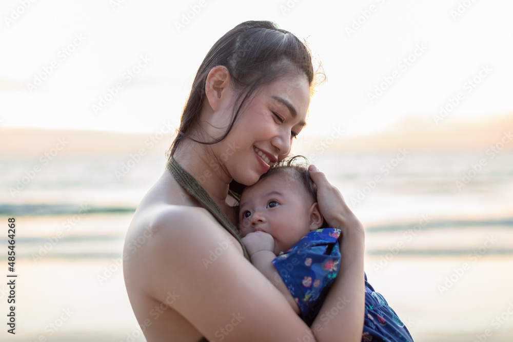 Beautiful Attractive Asian mom holding her baby newborn in hand and hugging baby sweet and lovely outdoor on the beach.Happy mother and infant baby looking together smile with natural sunset Beautiful Attractive Asian mom holding her baby newborn in hand and hugging baby sweet and lovely outdoor on the beach.Happy mother and infant baby looking together smile with natural sunset
