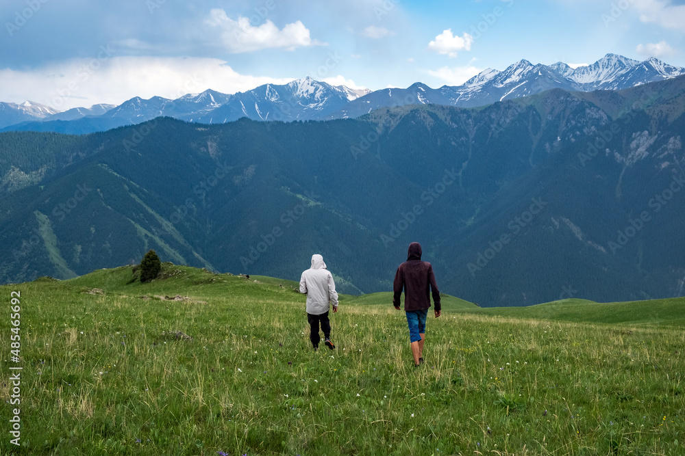 Tourist is walking on green valley with beautiful mountains background. People lifestyle concept. Chilik river valley. Travel, tourism in Kazakhstan concept. Trans-Ili Alatau mountains.