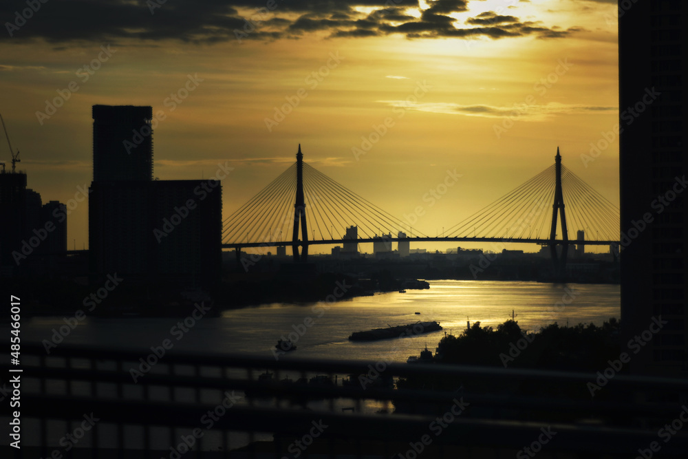 Fototapeta premium Good morning in city life concept. Silhouette of suspension bridges in bangkok city and building cross rivers are constructed in urban areas and buildings built near the river.