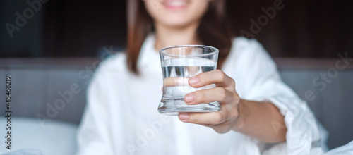 Obraz na plátně Happy woman holding water glass, female drinking pure water on bed at home
