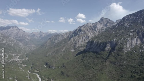 Frontal drone video moving over the Lumi i thethit river in sh21, albania, with the mountains in front as the main shot. Clear sky with few clouds. Town houses are visible. photo