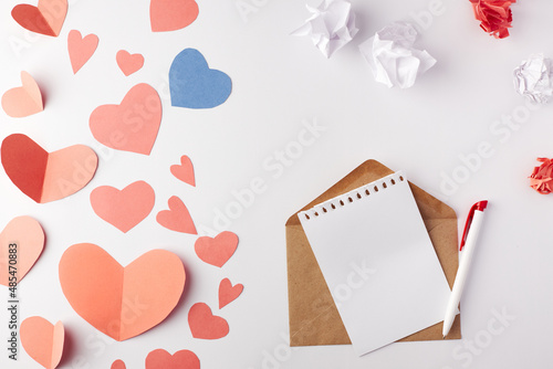 Valentine's Day, a note with an envelope and a pen between a large number of paper hearts. Top view. Copy space. Place for text.