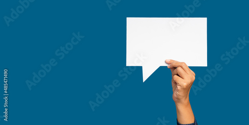 A speech bubble concept. Hand holding of an empty white speech bubble against a blue background.