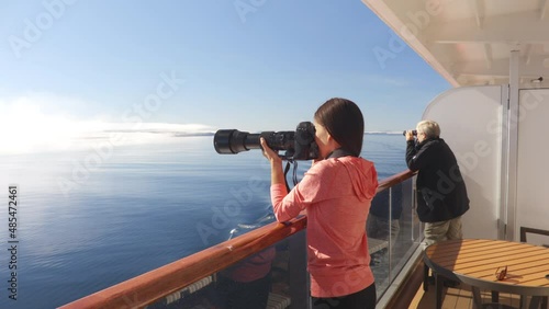 Cruise Ship Alaska Glacier Bay Tourists looking at landscape from private balcony suite stateroom cabin using telelens camera and binoculars. People on vacation travel looking at wildlife cruising photo