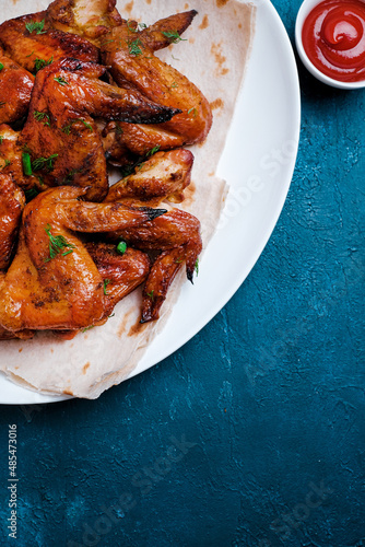 White plate of barbecue chicken wings on blue background. Top view.
